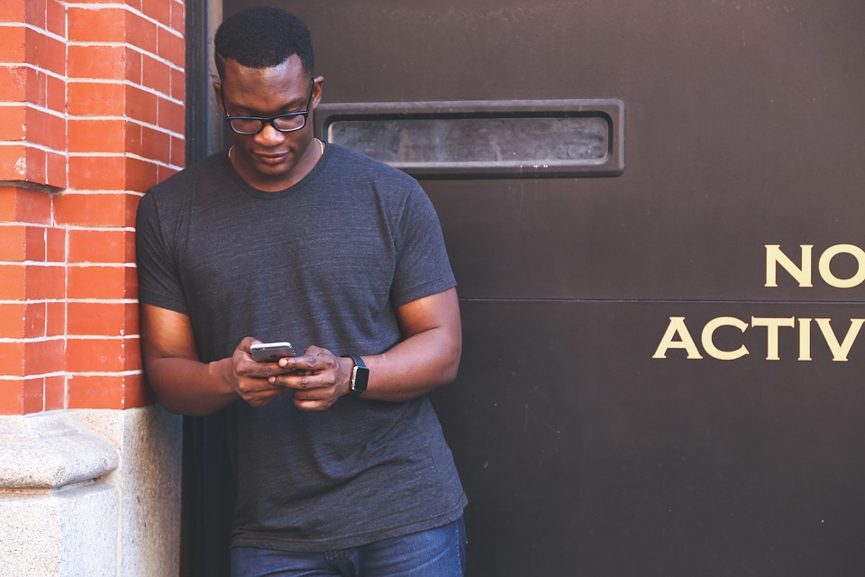 A man leaning on the wall texting someone on her mobile phone